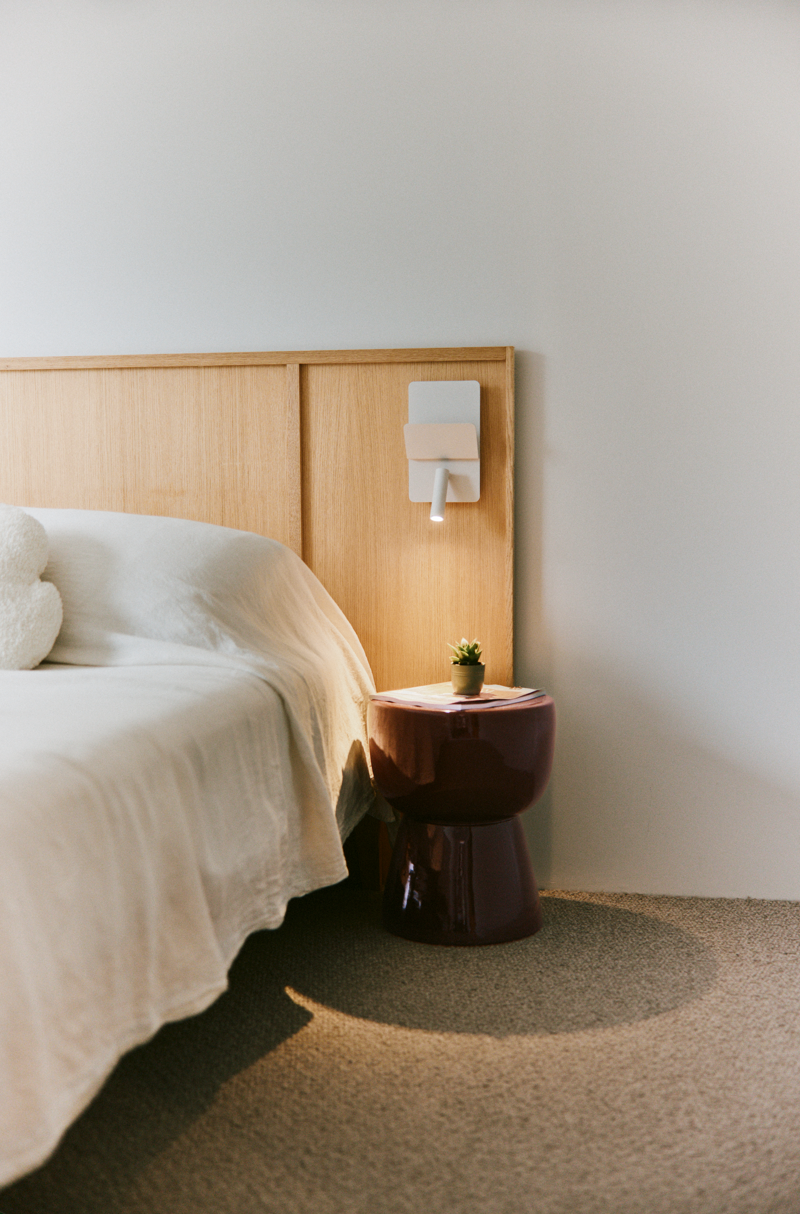 Bedroom with a light wood headboard and burgundy side table, interior design by M La Déco, Basque Country