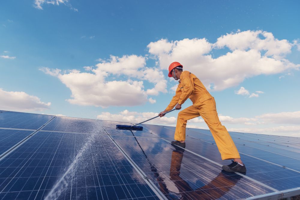 Person in Orange Overalls Cleaning Solar Panels on a Rooftop — LSEA Electrical Group in Bucasia, QLD