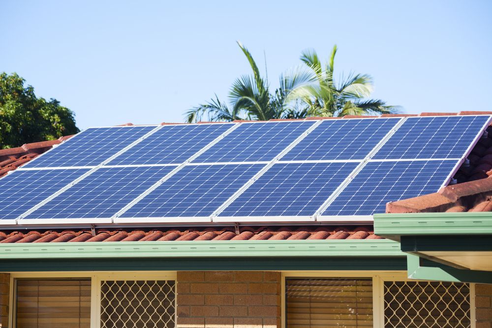 Solar Panels on a Red Tile Roof of a House With Palm Trees and Blue Sky — LSEA Electrical Group in Paget, QLD