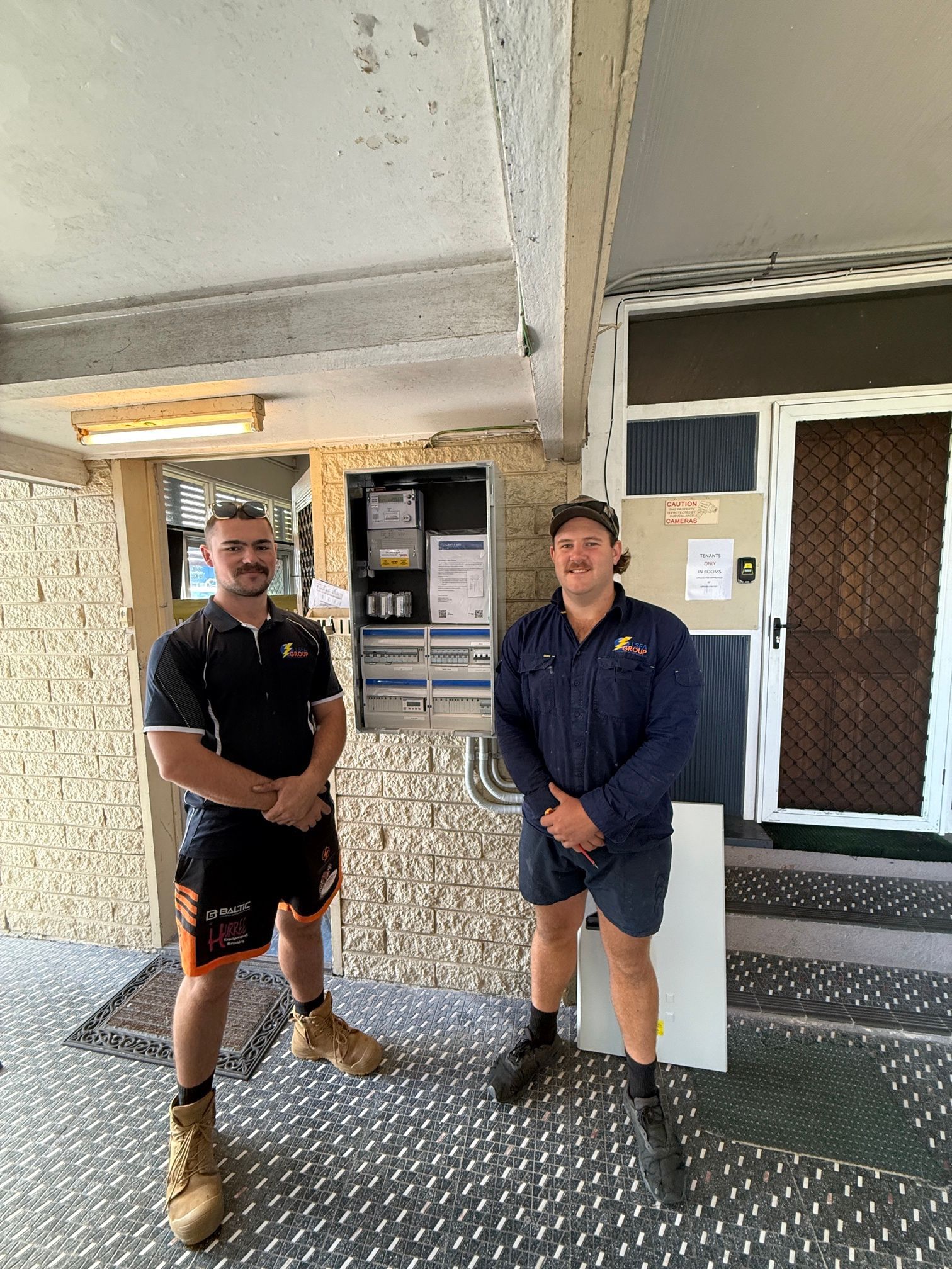 Two people standing outside a building entrance on a covered walkway, smiling at the camera — LSEA Electrical Group in Bucasia, QLD