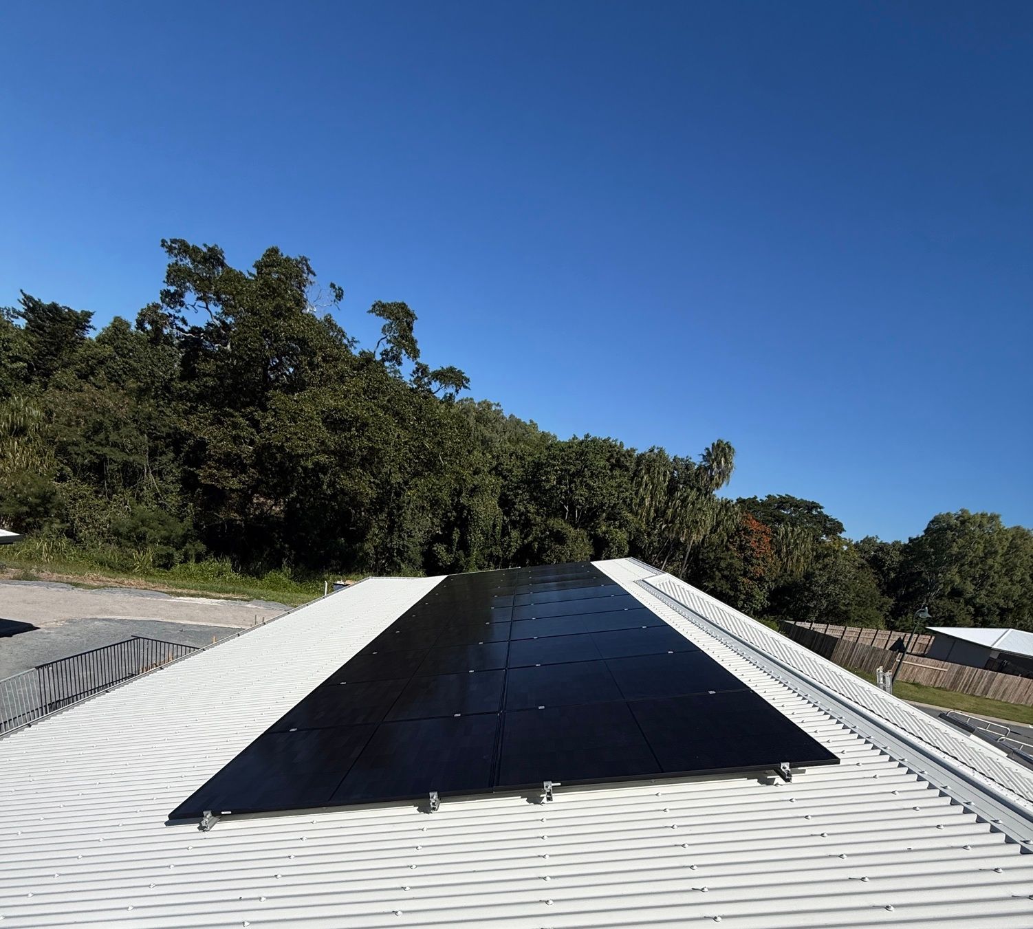 Solar panel on a white corrugated roof under a clear blue sky, with trees in the background — LSEA Electrical Group in Bucasia, QLD