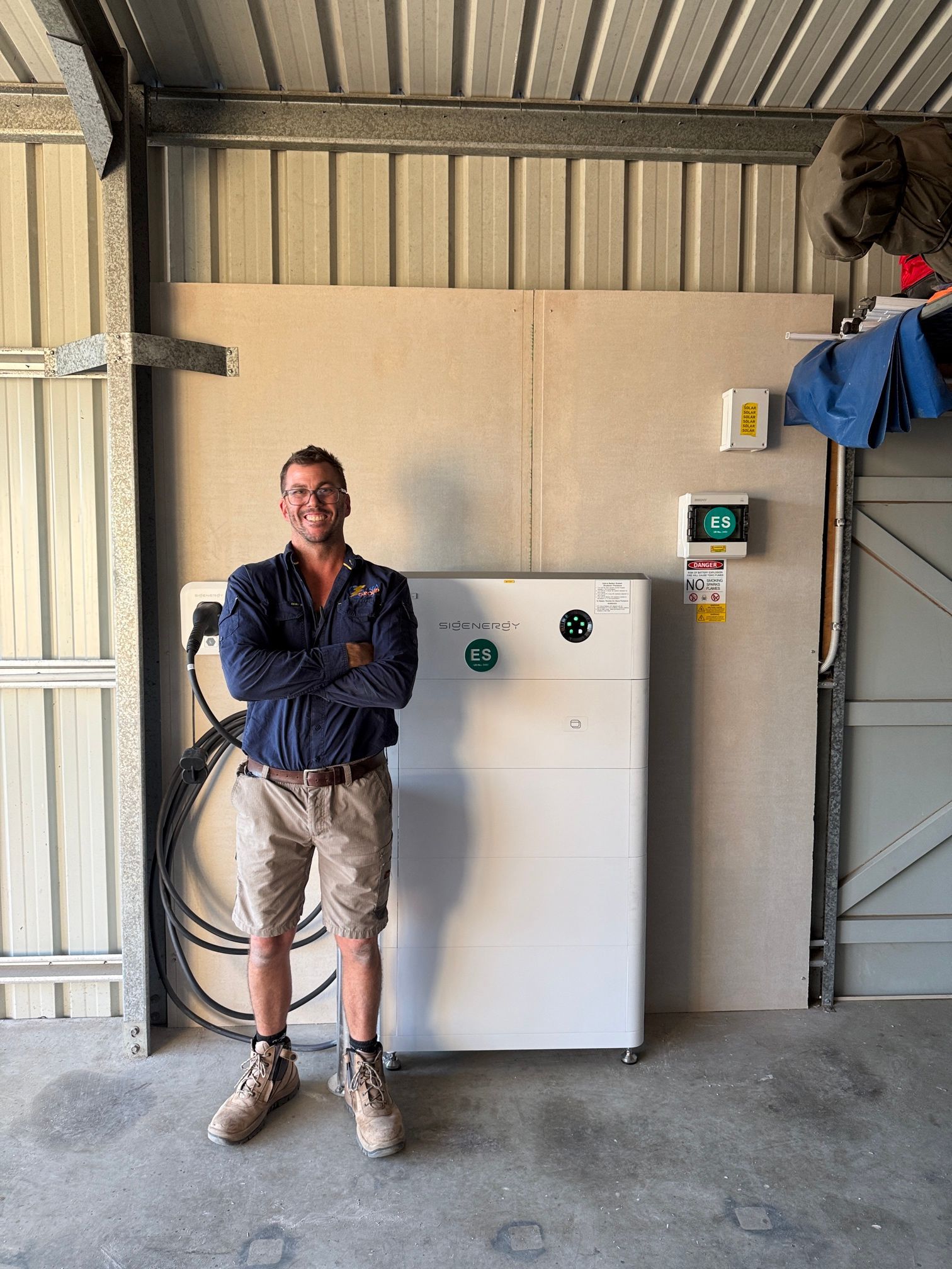 Man standing beside a large white electrical panel in an industrial room, arms crossed and smiling — LSEA Electrical Group in Bucasia, QLD