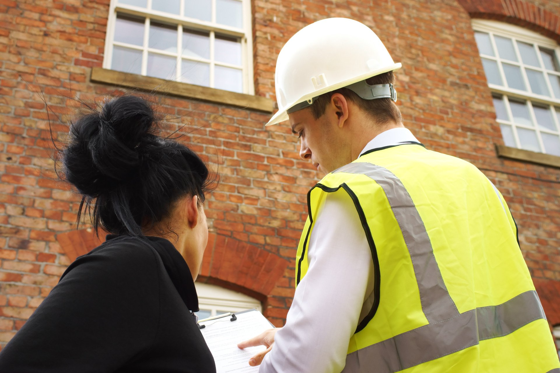 a man and a woman are looking at a clipboard in front of a brick building