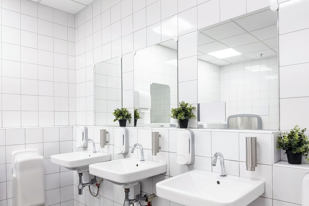Bright white tiled bathroom with two sinks, mirrors, and small potted plants