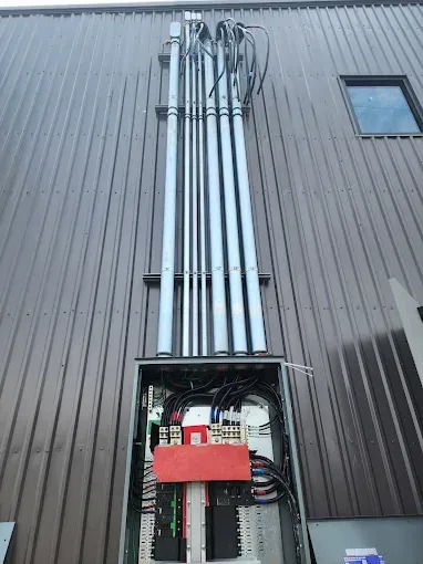 Exterior wall with exposed utility conduits and an open electrical panel with red cover on a building.