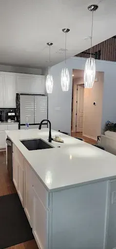 Modern kitchen with white island, black sink, pendant lights, and gray cabinets