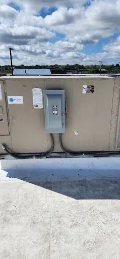 Outdoor utility equipment with a gray electrical panel mounted on a tan wall under a cloudy sky