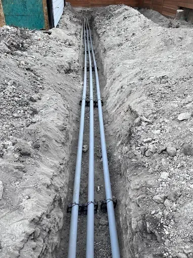 Gray utility conduits laid in a trench between dirt banks at a construction site