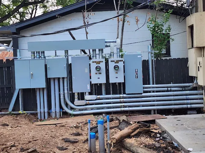 Outdoor utility electrical panels and gray conduit pipes beside a building wall
