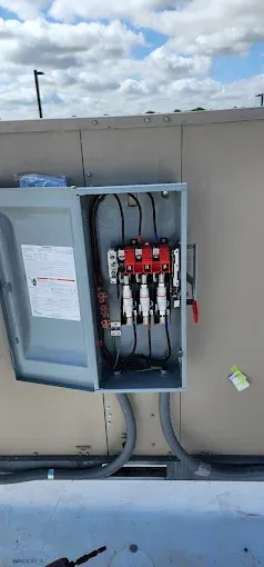 Open electrical breaker panel mounted on an exterior wall with red components and visible conduit.