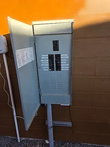 Open electrical breaker panel on an exterior wall with the door ajar.