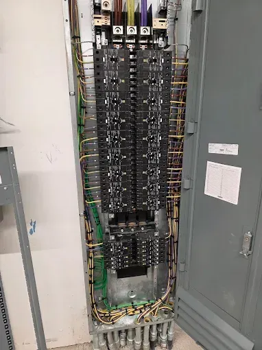 Open electrical breaker panel with rows of circuit breakers and exposed wiring in a utility closet