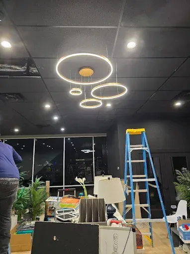 Office under renovation with ladder, tools, plants, and circular ceiling lights against black ceiling.