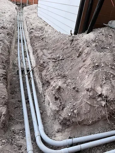Underground utility pipes laid in a dirt trench beside a building wall