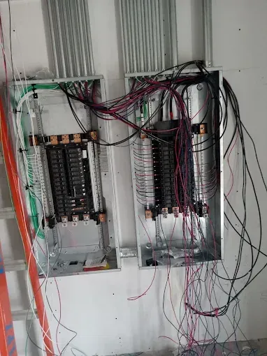 Open electrical panel with tangled exposed wiring and circuit breakers on a wall