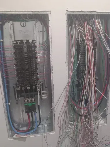 Two open electrical breaker panels with exposed, tangled wiring in a wall recess