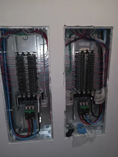 Two open electrical breaker panels mounted side by side on a wall, with exposed wiring and circuits.