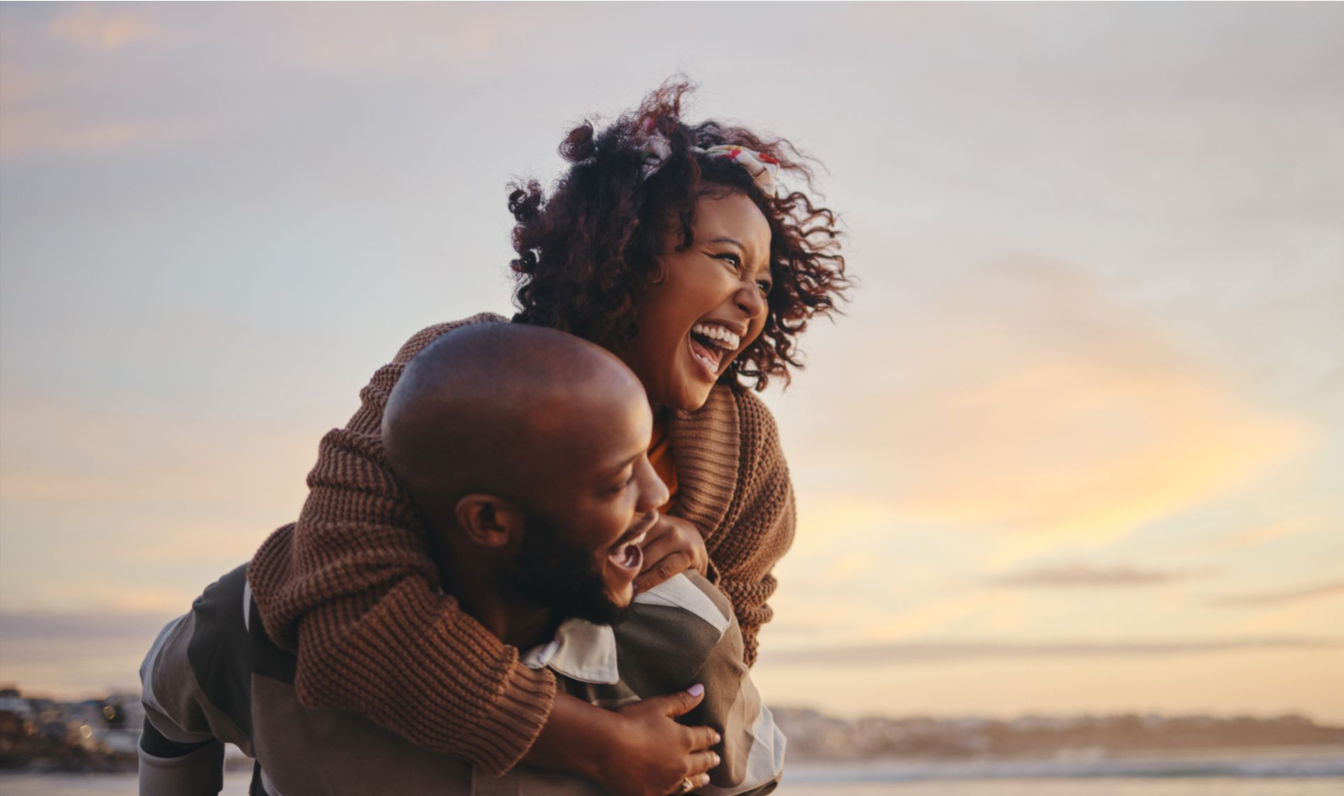 Man carrying a woman on his back as they are both smiling.