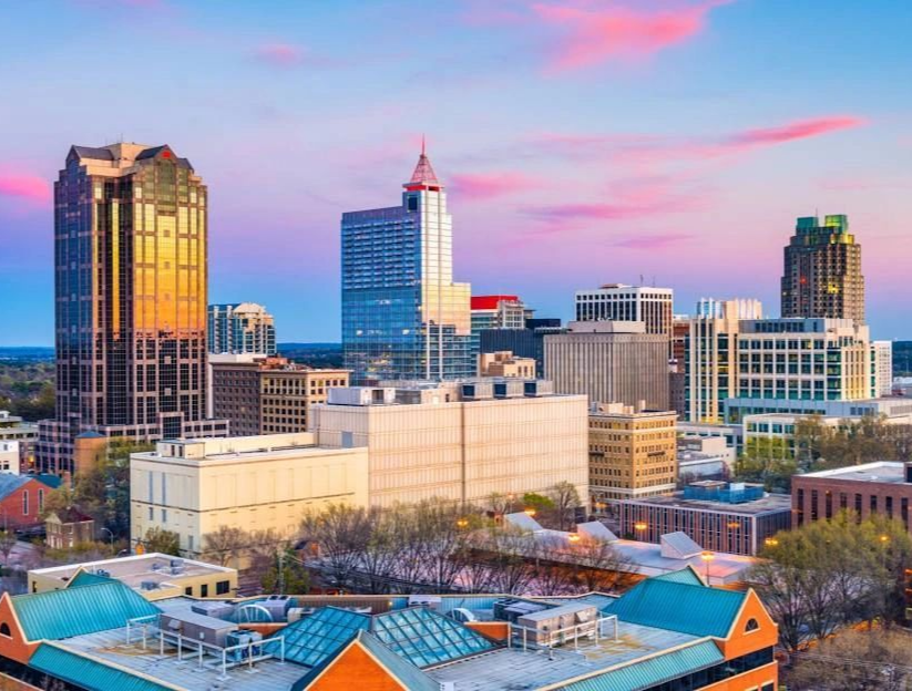 Downtown Raleigh skyline at sunset, featuring prominent skyscrapers against a purple and orange sky.