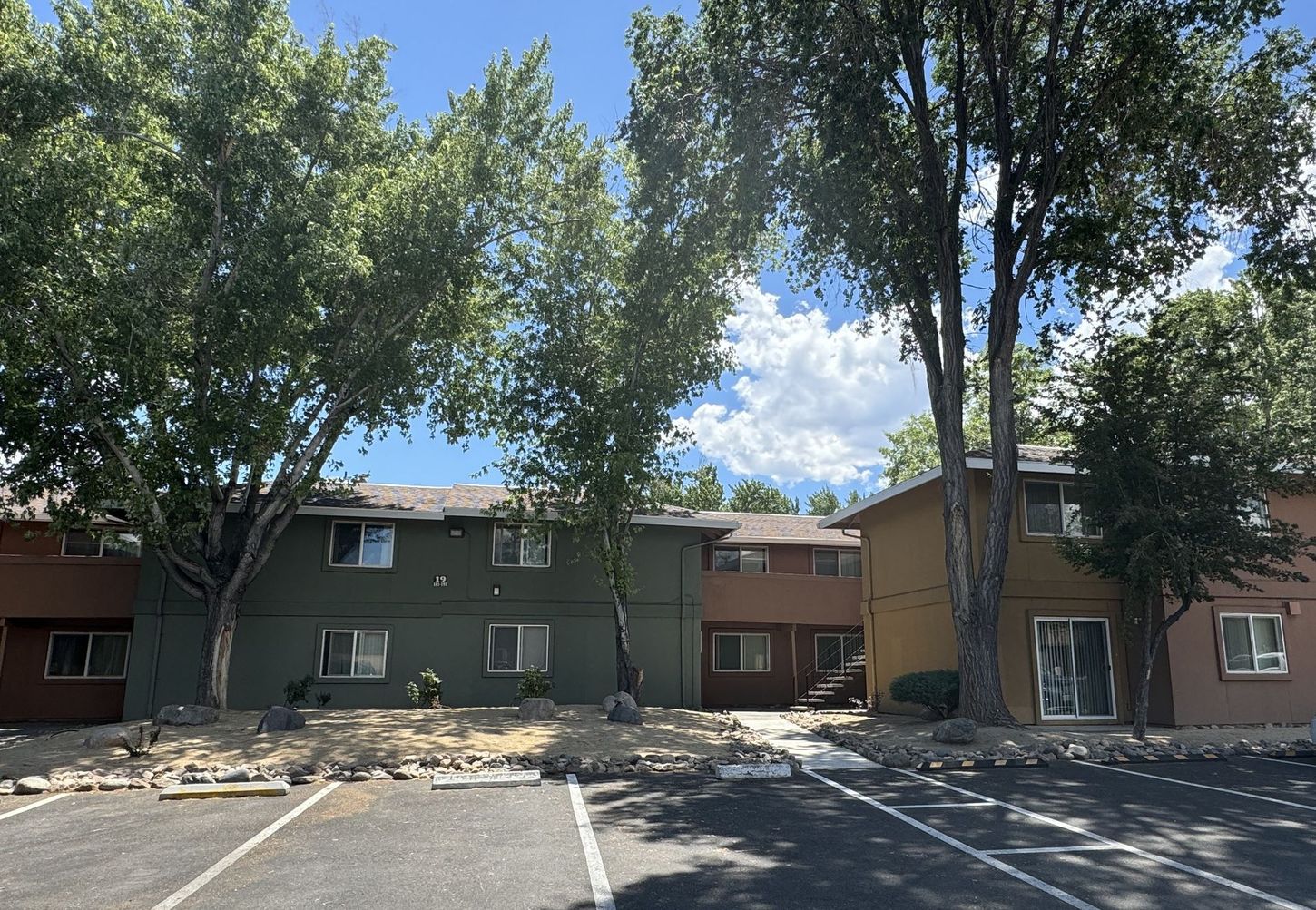 Apartment complex with multiple buildings in various earth-tone colors and trees in front on a sunny day.