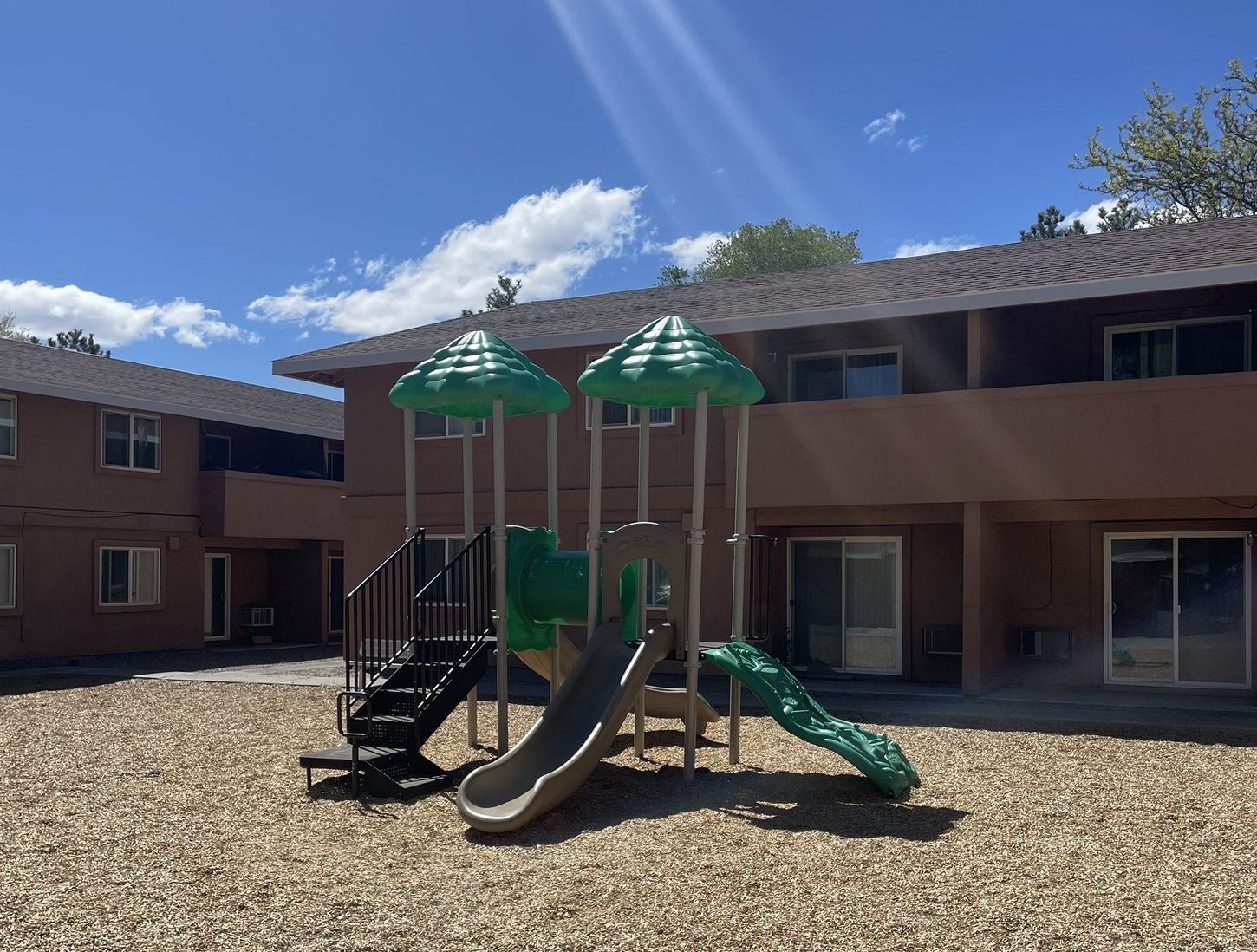 Playground in a courtyard between two brown apartment buildings on a sunny day.
