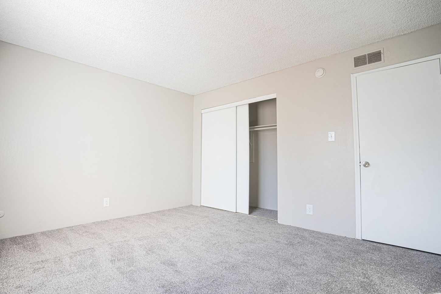 Empty bedroom with gray carpet, two white doors, and a closet.
