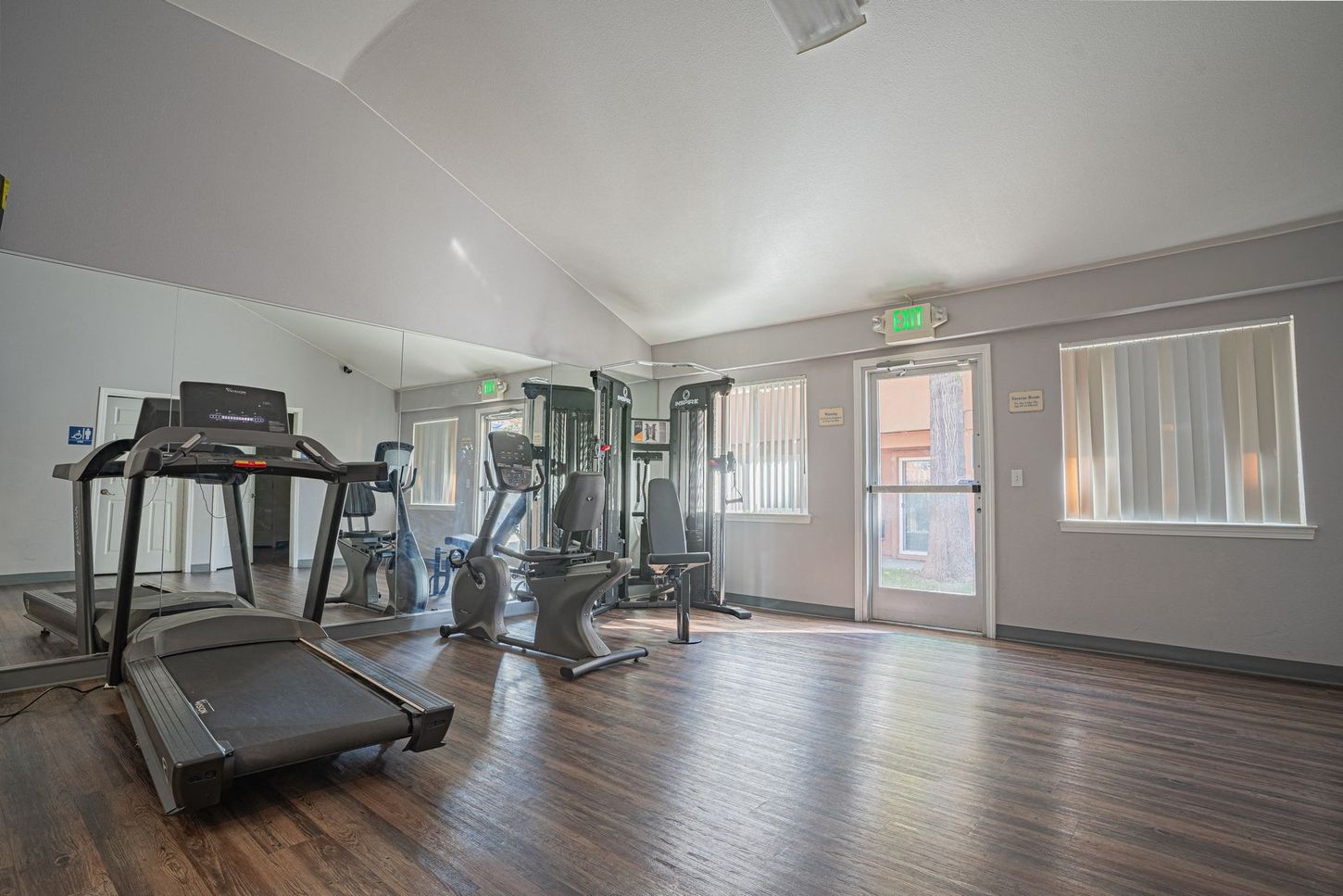 Gym with treadmills, stationary bikes, and weight machines on wood floor.