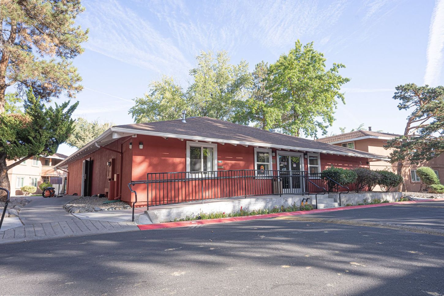 Red building with ramp and sidewalk access, surrounded by trees and a parking area.