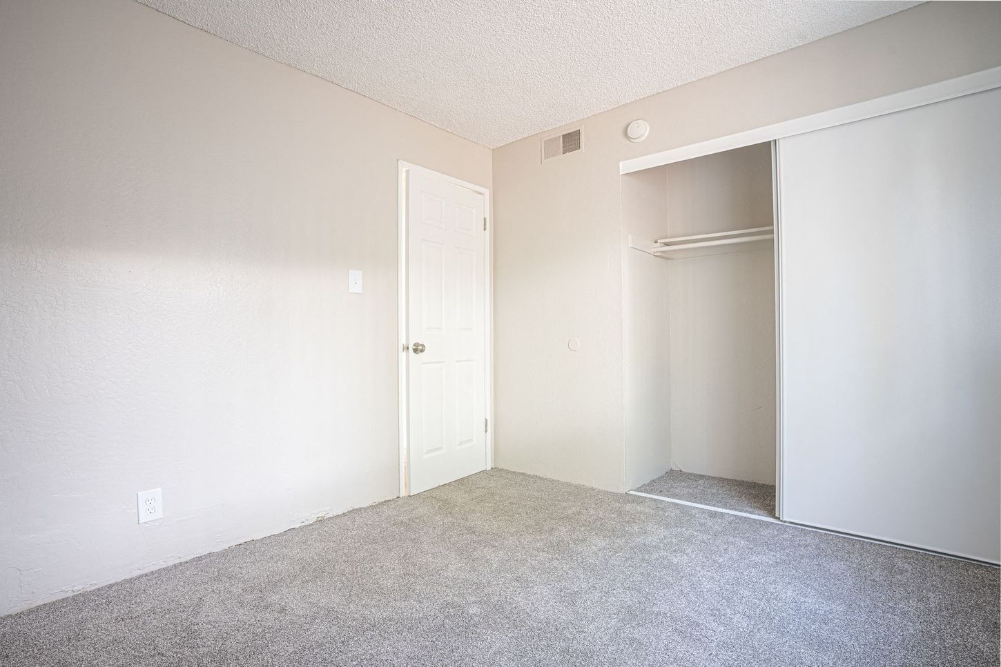 Empty bedroom with gray carpet, white walls, closet, and a closed door.