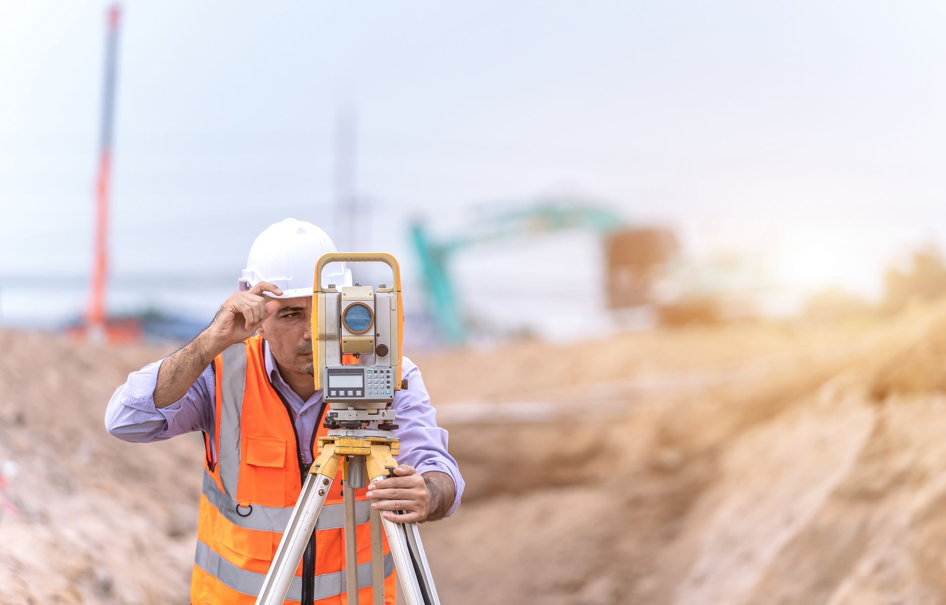 A construction worker is using a theodolite on a construction site.