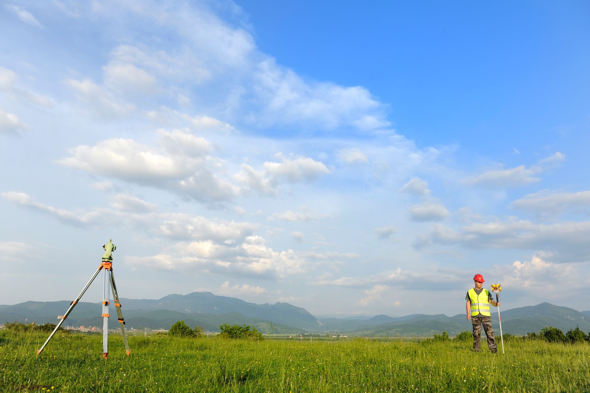 Land surveyor wearing a reflective uniform, working a total station in nature.