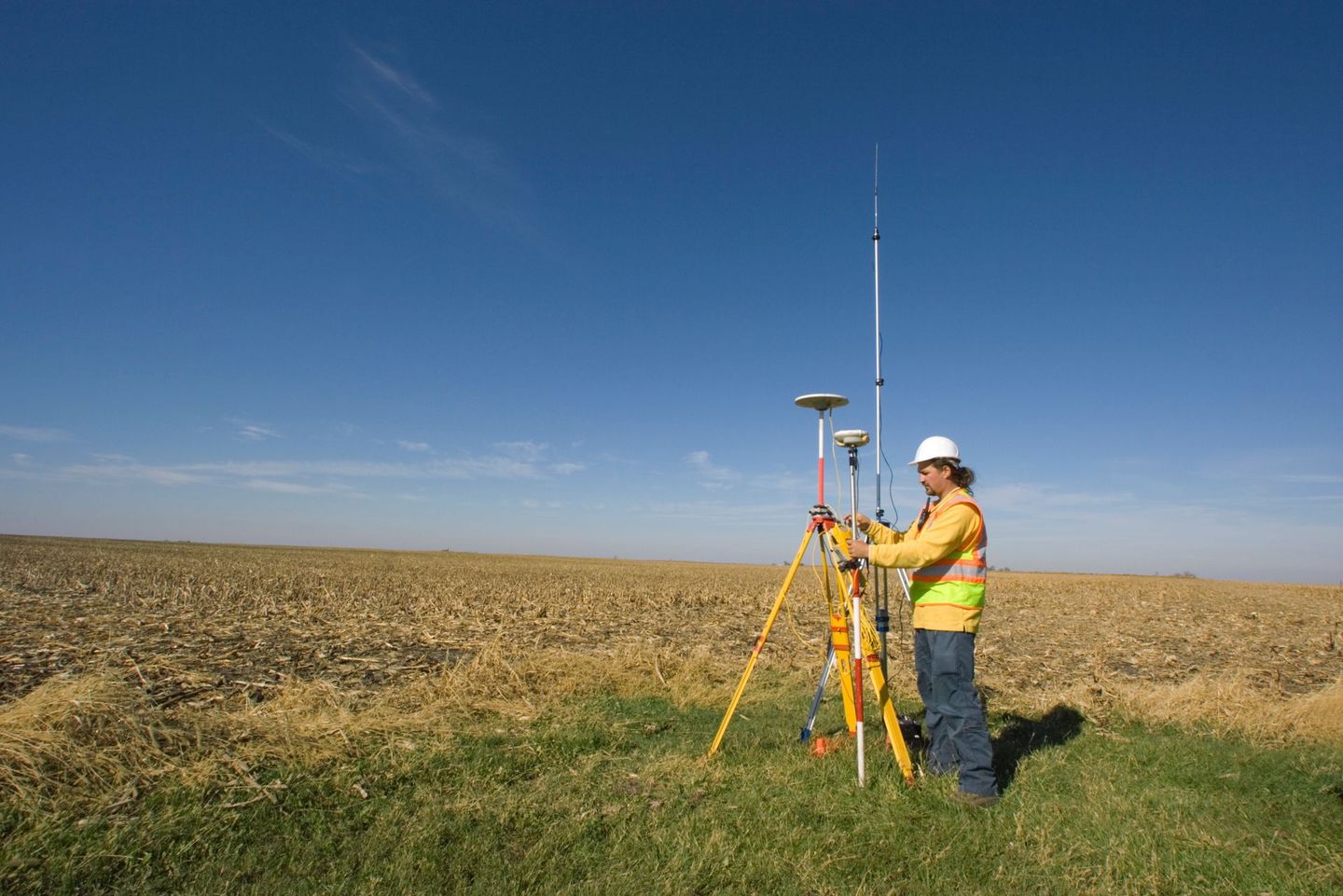 A man is standing in a field with a tripod and a satellite dish.