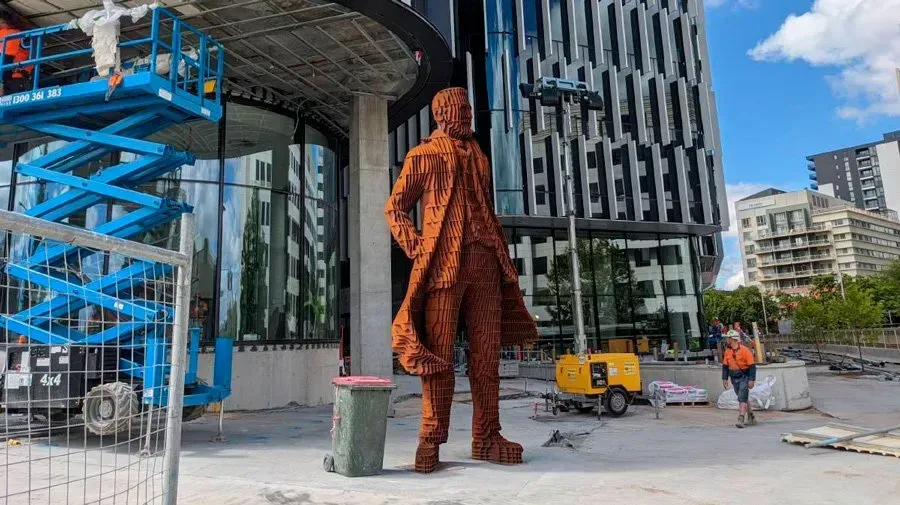 A statue of a man is standing in front of a building under construction.