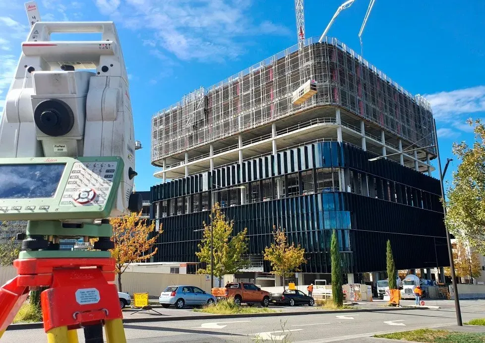 A construction site with a building under construction and a total station in front of it.