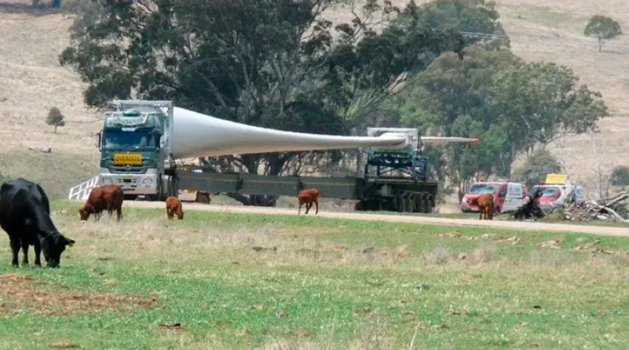 A truck is carrying a large wind turbine blade on a trailer.
