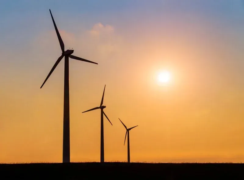 Three wind turbines are silhouetted against a sunset sky.