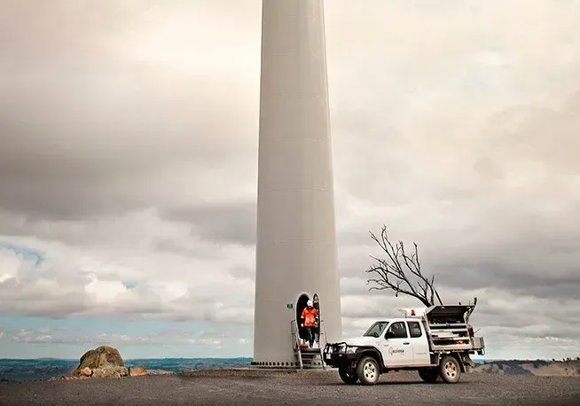 A white truck is parked in front of a wind turbine.