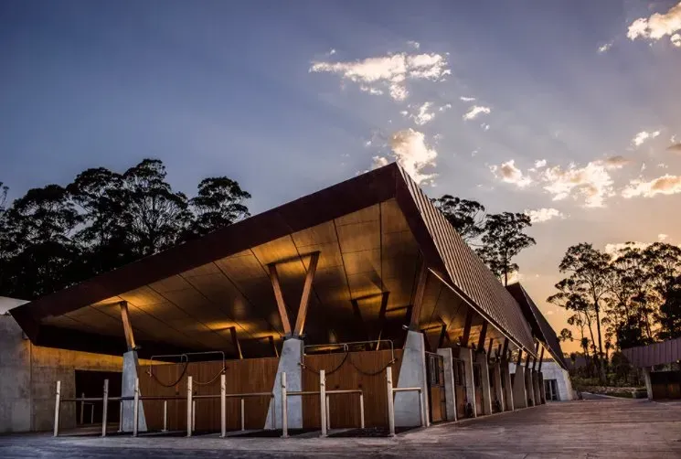 A large building with a roof that looks like a pyramid is surrounded by trees at sunset.
