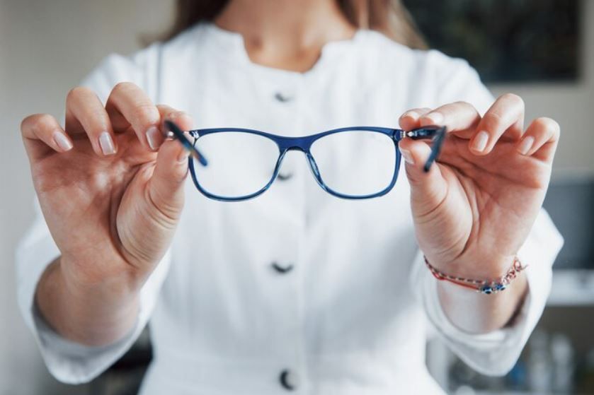 Persona sosteniendo gafas azules frente a un fondo de camisa blanca borrosa.