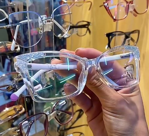 Una mano sostiene unas monturas de gafas transparentes en el escaparate de una óptica.
