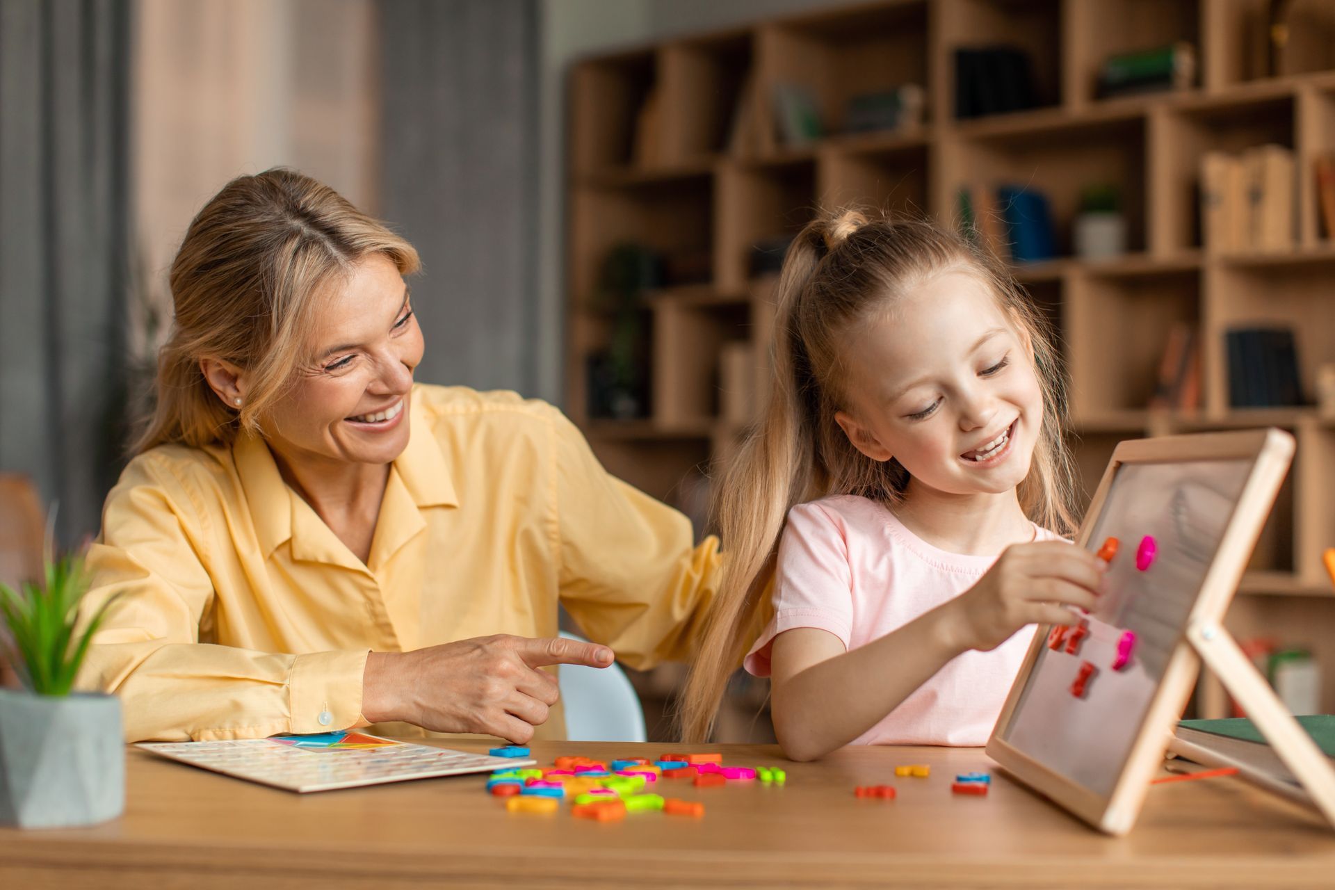 A woman and a little girl are playing with a magnetic board.