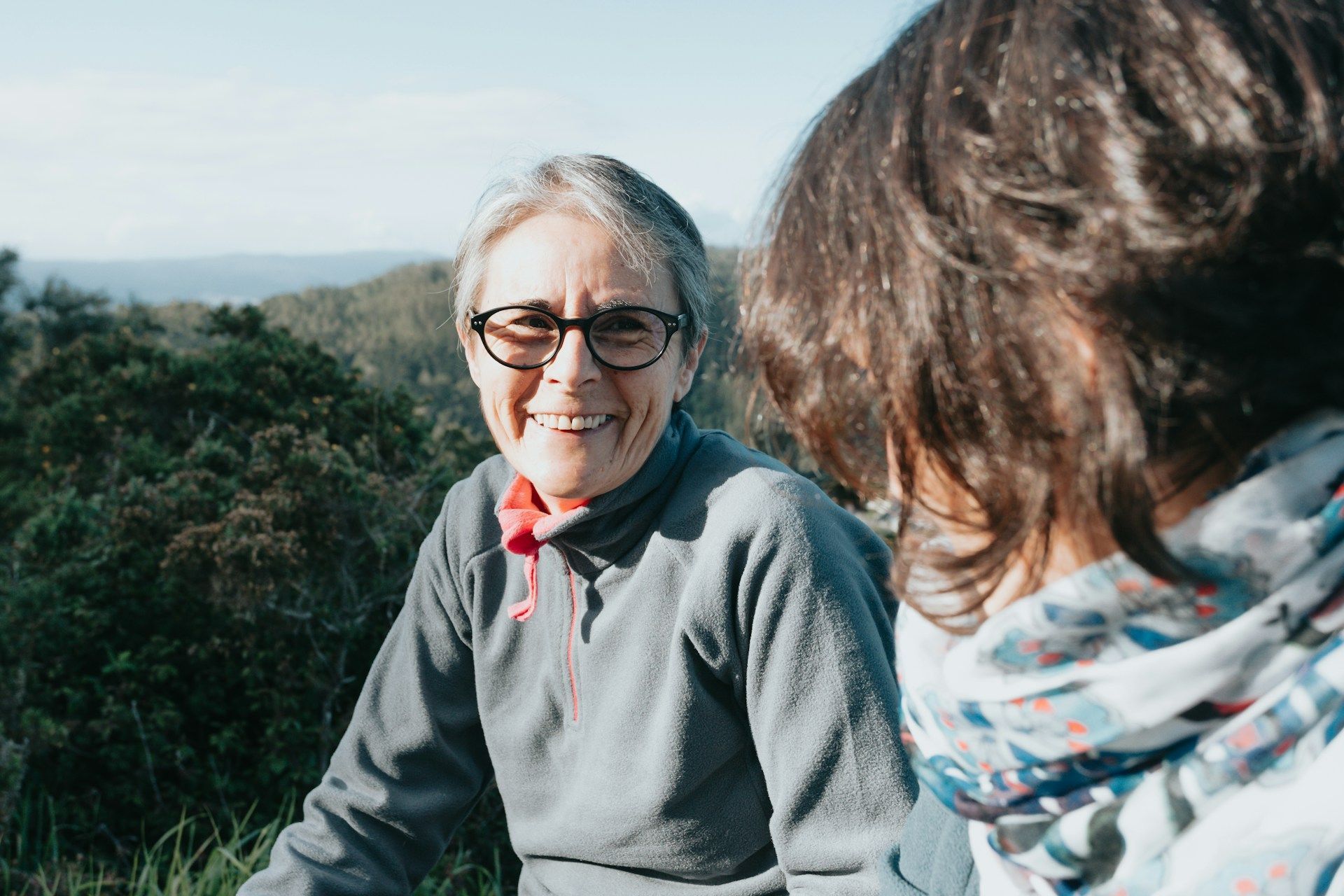 A woman wearing glasses is sitting in the grass with another woman.