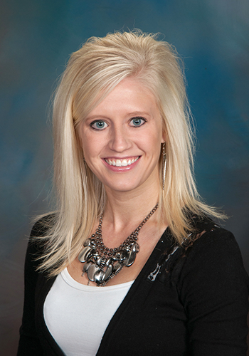 A woman wearing a black sweater and a necklace is smiling for the camera.