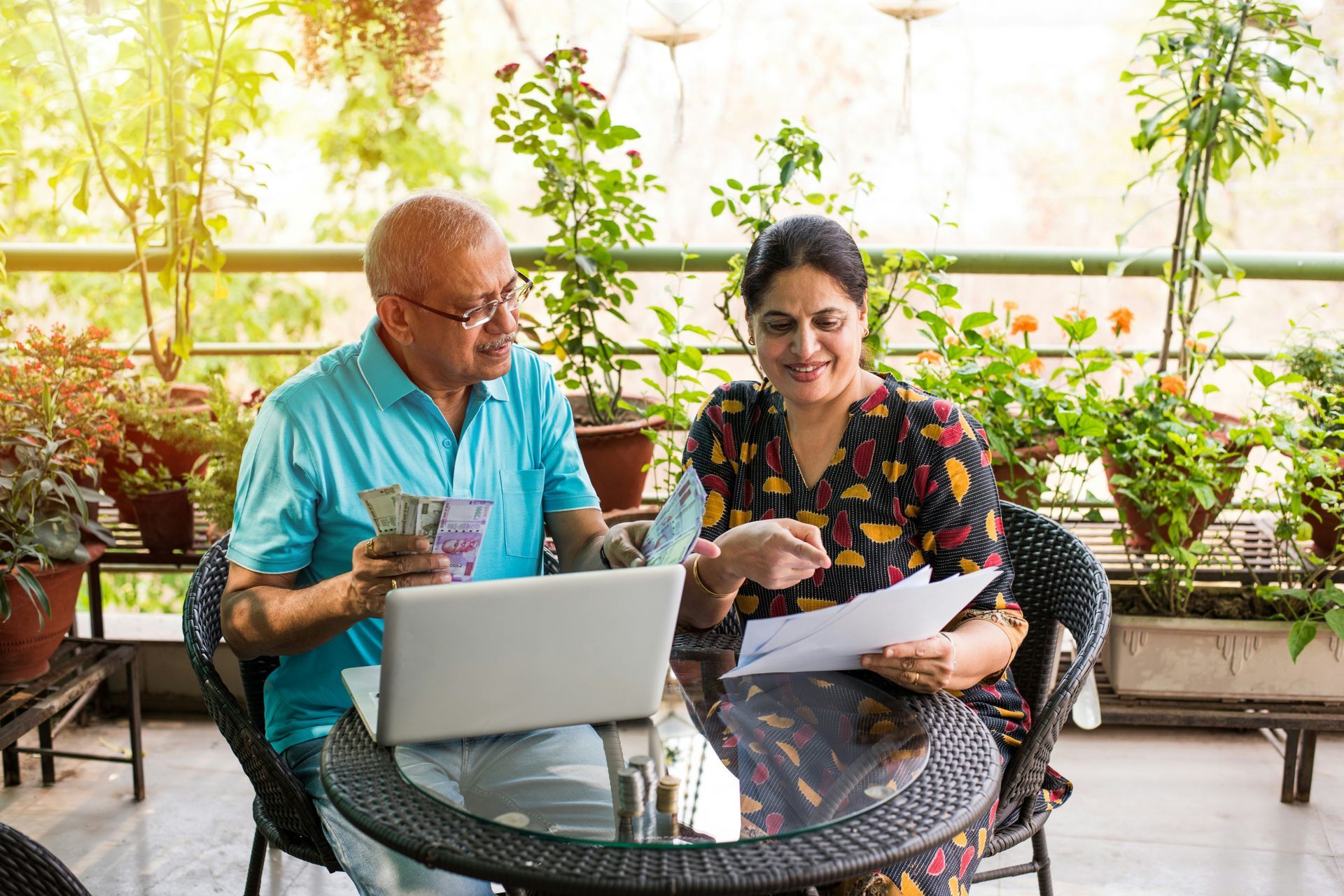 A man and a woman are sitting at a table looking at a laptop.