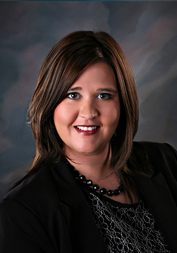 A woman wearing a black jacket and a necklace smiles for the camera