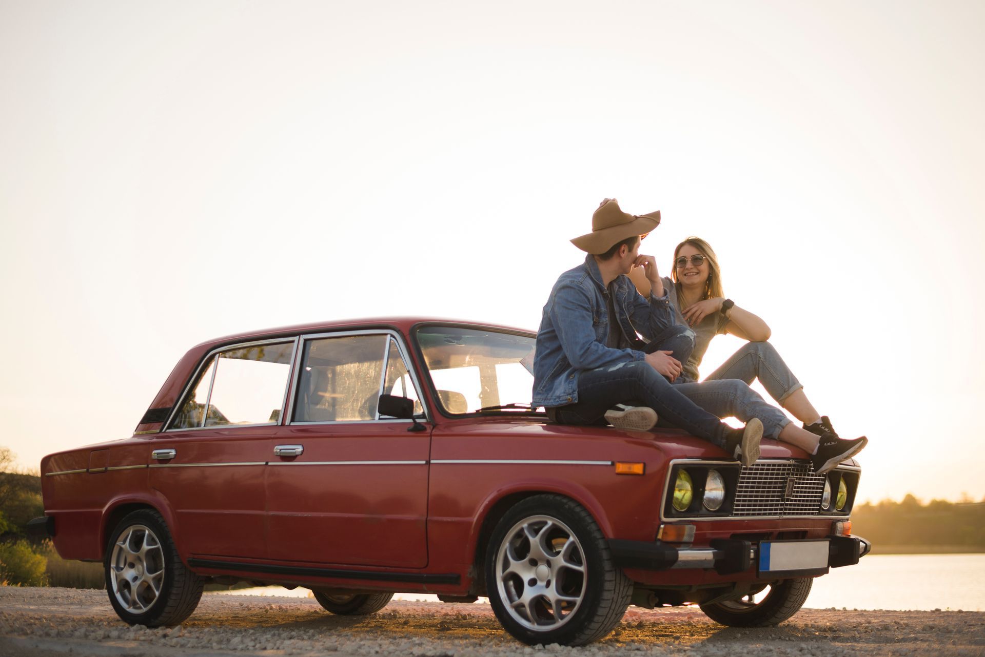A man and a woman are sitting on the roof of a red car.