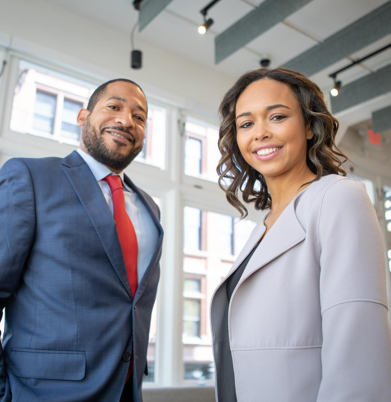 A man in a suit and tie stands next to a woman in a grey jacket