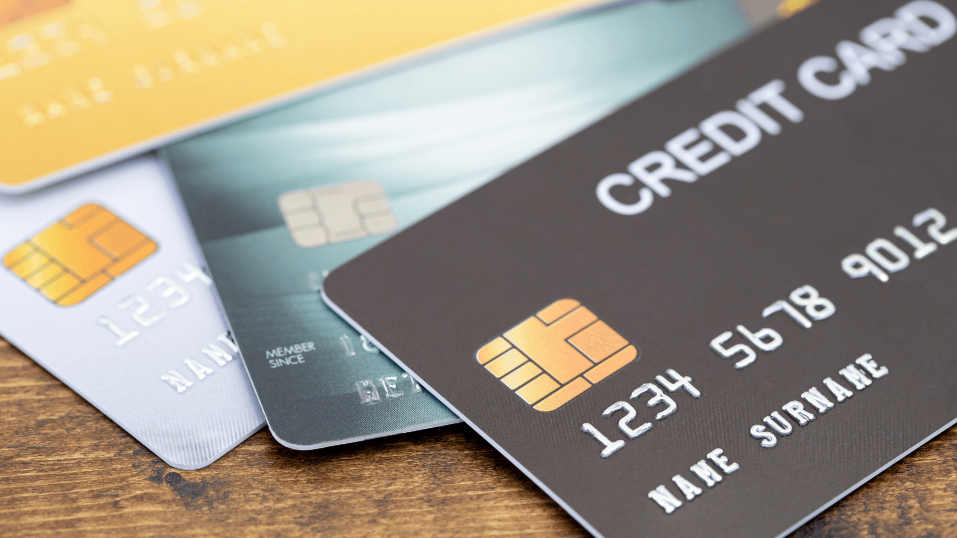 Three credit cards are stacked on top of each other on a wooden table.