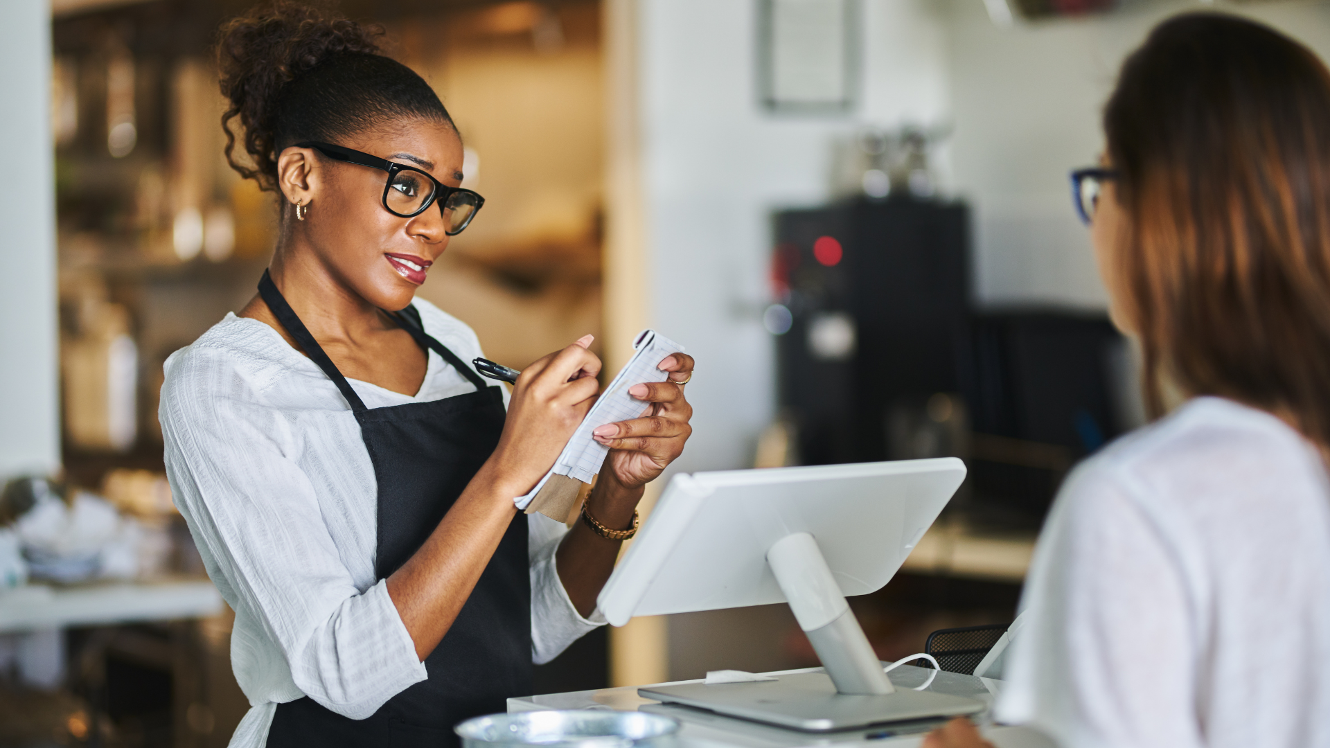 A woman is taking a order from a customer at a restaurant.