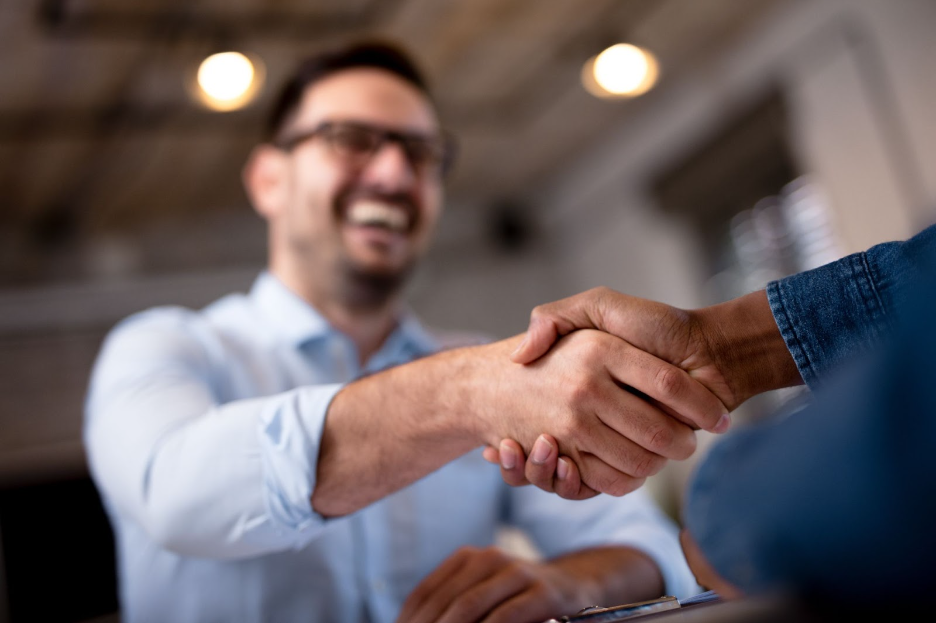 A man is shaking hands with another man while sitting at a table.